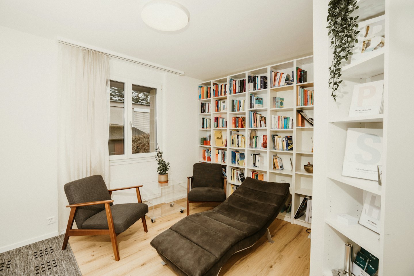 Gemütliches Therapiezimmer mit Sesseln, Chaiselongue und Bücherregalen.